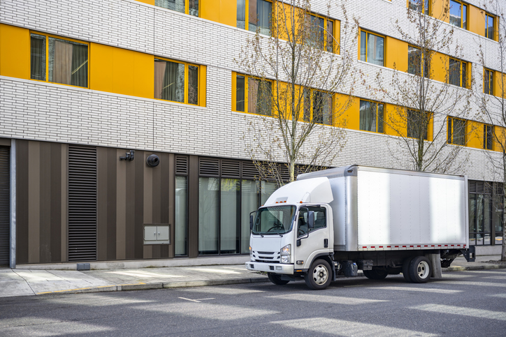 White box truck parked on the street in front of a modern building with yellow window panels.