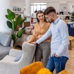 Couple in a furniture showroom smiling while inspecting a light gray armchair.