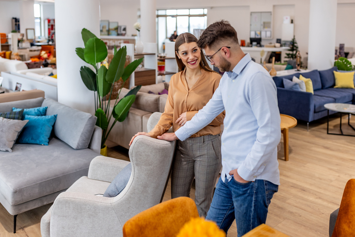 Couple in a furniture showroom smiling while inspecting a light gray armchair.